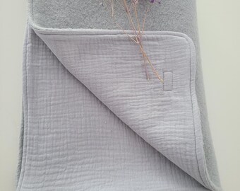 May include: A soft, light gray baby blanket with a textured muslin side and a soft fleece side. The blanket is folded in half and has a small tag with the text "Tater Tot" on it.