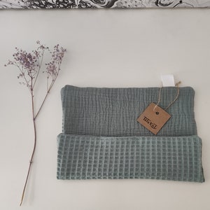 Puede incluir: Un pa&ntilde;o de cocina de tejido de gofre verde salvia con una capa superior de muselina a juego. El pa&ntilde;o de cocina tiene una etiqueta marr&oacute;n con la palabra "Tillex" escrita en ella.