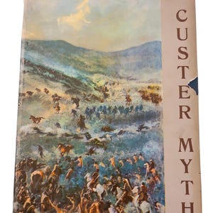 Peut inclure: Un livre vintage intitulé "The Custer Myth" par Graham. La couverture présente une peinture détaillée d'une scène de bataille avec des chevaux et des personnages en action, sur fond de collines et de ciel nuageux. Le livre montre des signes d'usure.
