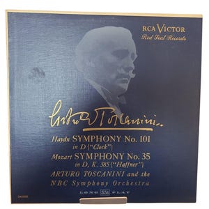 May include: Vintage vinyl record album cover featuring a portrait of Arturo Toscanini. The album is titled "Haydn Symphony No. 101" and "Mozart Symphony No. 35". The cover is dark blue with gold lettering and the RCA Victor Red Seal Records logo.