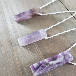 May include: Three amethyst crystal pendants on white cords. The crystals are all different shapes and sizes, but they are all a beautiful shade of purple.