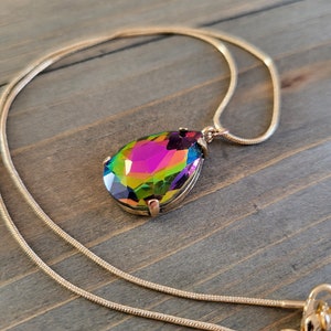 May include: A gold chain necklace with a large iridescent teardrop pendant. The pendant has a faceted design and reflects multiple colors.