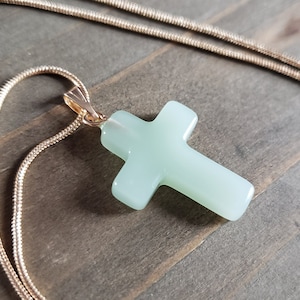 May include: A delicate gold chain necklace with a light green jade cross pendant.