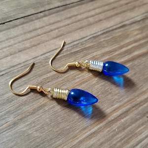 Könnte beinhalten: Ein Paar blaue Glühbirnen-Ohrringe mit goldenen und silbernen Akzenten. Die Ohrringe sind im Hänge-Stil mit einem Hakenverschluss.