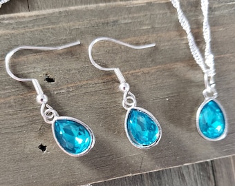 May include: A silver necklace and earrings set with teardrop-shaped turquoise blue crystals.
