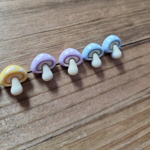 May include: A row of colorful mushroom-shaped objects. The mushrooms have white stems and caps in yellow, lavender, light blue, and blue, each with white polka dots. The objects are arranged on a wooden surface.