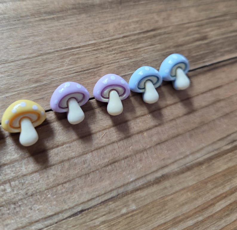 May include: A row of colorful mushroom-shaped objects. The mushrooms have white stems and caps in yellow, lavender, light blue, and blue, each with white polka dots. The objects are arranged on a wooden surface.