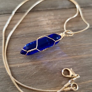 以下が含まれることがあります： 金色のチェーンネックレスに、金色のワイヤーで包まれた青いガラスのペンダントがついたもの