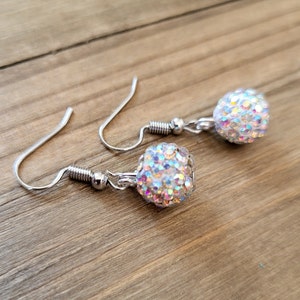 May include: A pair of silver earrings with white iridescent crystal ball charms. The earrings have a simple hook design.