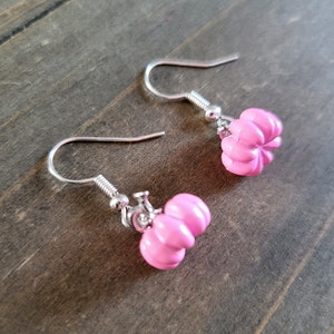 May include: A pair of silver earrings with pink pumpkin charms. The pumpkins have a ribbed texture and are a light pink color.