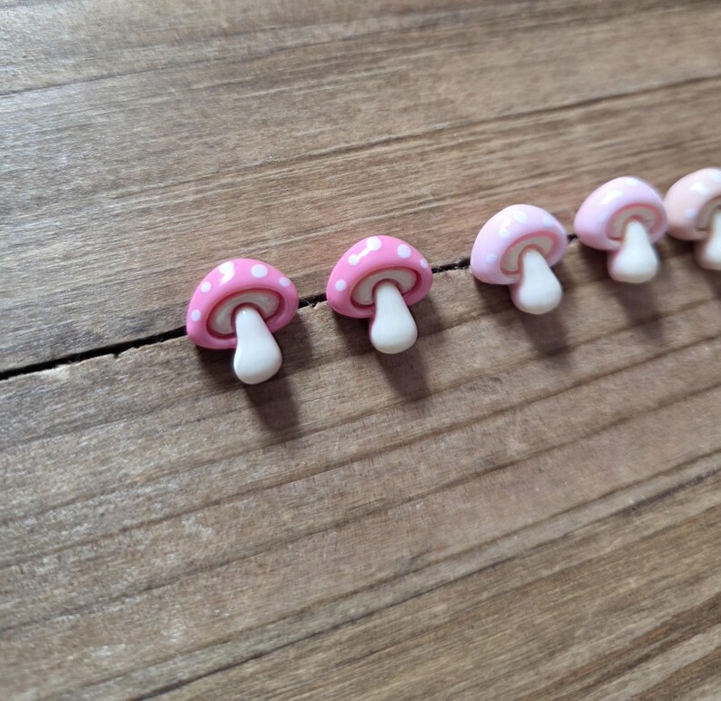 May include: A row of small, pink mushroom-shaped decorative items with white polka dots on the caps and white stems. The mushrooms are arranged on a wooden surface, creating a whimsical and playful aesthetic.