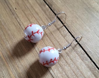 May include: A pair of silver dangle earrings with white ceramic baseball charms. The charms have red stitching details.