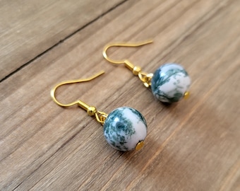 May include: A pair of gold dangle earrings with green and white agate stone beads. The beads have a marbled pattern.