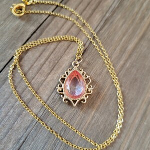 May include: A gold chain necklace with a pink teardrop-shaped pendant set in a gold filigree frame.