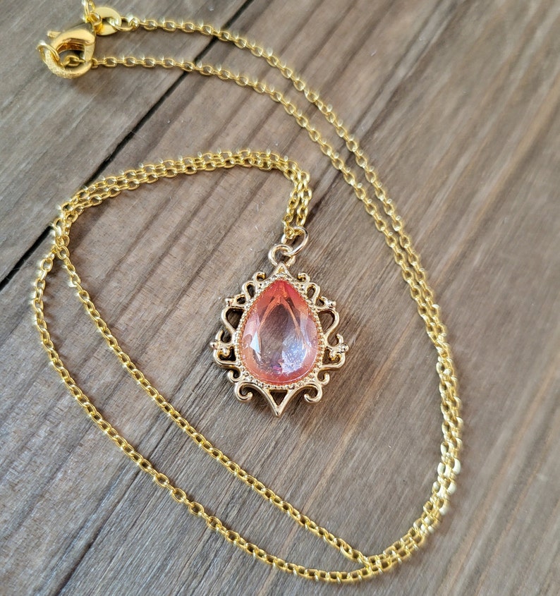 May include: A gold chain necklace with a pink teardrop-shaped pendant set in a gold filigree frame.
