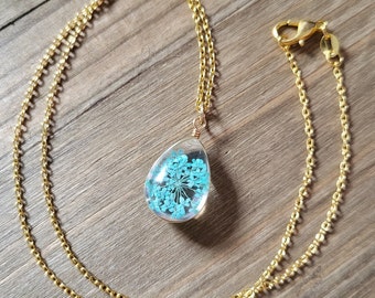May include: A gold chain necklace with a teardrop-shaped pendant containing a pressed blue flower.