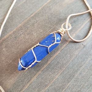 Op de afbeelding: Een blauwe edelsteen hanger gewikkeld in gouden draad, hangend aan een gouden ketting.
