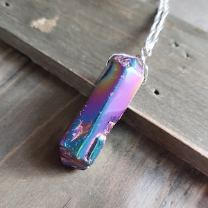 May include: A iridescent purple, blue, and green crystal pendant on a silver chain. The crystal is faceted and has a geometric shape.