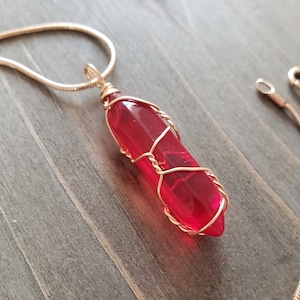 May include: A red glass pendant wrapped in gold wire, hanging from a silver chain necklace.