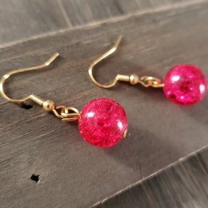 May include: A pair of gold dangle earrings with pink glass beads. The beads have a sparkly, textured finish.