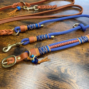 Könnte beinhalten: Drei Leder-Hundeleinen mit blauem und braunem geflochtenem Seil. Die Leinen haben Messingbeschläge und blaue und braune Perlen.