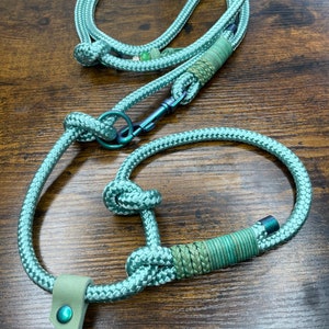 以下が含まれることがあります： 革製のハンドルと金属製の留め具が付いた、ティールブルーのロープ製の犬のリード。リードは結び目が付いており、緑とティール色の編み込み部分があります。