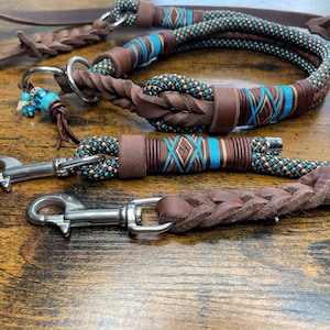Könnte beinhalten: Eine braune Lederhundeleine mit einer türkisfarbenen und braunen Seilleine. Die Seilleine hat ein türkisfarbenes und braunes geflochtenes Design. Die Leinen haben silberne Metallverschlüsse.
