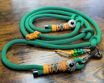 May include: A green rope dog leash with decorative accents. The leash features a silver clasp, a decorative leather accent, and a silver embellishment with a black center. The leash is made of a thick, durable rope.