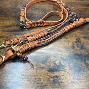 Könnte beinhalten: Ein Hundeleinen- und Halsbandset aus hellbraunem Leder und dunkelbraunem Seil mit aufwendigen Flechtdetails, Messingbeschlägen, Metallnieten und dekorativen Perlen. Das Set enthält einen passenden Griff, eine verstellbare Schnalle und Karabinerhaken.