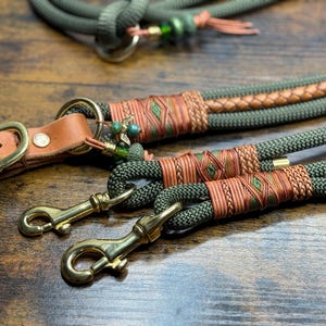 Könnte beinhalten: Nahaufnahme eines Hundeleinen- und Halsband-Sets. Das Set besteht aus olivgrünem Seil mit hellbraunen Lederakzenten und Messingbeschlägen. Die Leine hat einen geflochtenen Lederabschnitt und dekorative Nähte.