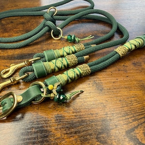 Könnte beinhalten: Ein Set aus grünen Hundeleinen und einem passenden Halsband mit goldfarbener Hardware. Die Leinen bestehen aus dickem, geflochtenem Seil und weisen dekorative gold- und grüne Akzente auf. Das Halsband hat eine goldene Schnalle.