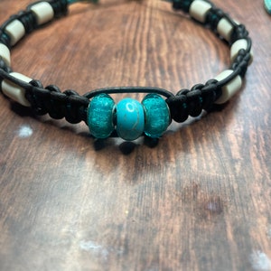 Könnte beinhalten: Ein schwarzes Lederarmband mit weißen Perlen und türkisfarbenen Glasperlen.