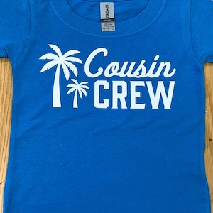 May include: A bright blue t-shirt with a white design of two palm trees and the text "Cousin Crew".