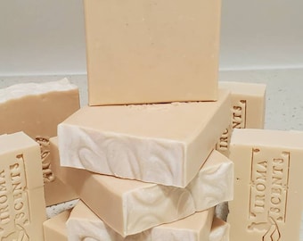 May include: A stack of light beige rectangular soap bars with a swirled white pattern on the top edges. Some bars have the text "IROMA SCENTS" carved into them. The soaps are arranged on a light-colored surface.
