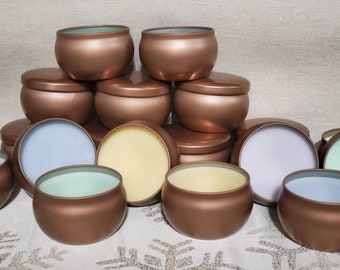 May include: A collection of small, round, copper-colored candle tins with various colored waxes inside. The candles are arranged in a pyramid shape.