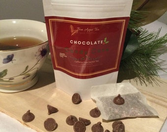 May include: A white pouch of "Bon Appé Tea" Chocolate Candy Cane herbal tea with a red label, a teacup, and chocolate chips on a wooden board. The tea bag and chocolate chips are visible. Caffeine-free.