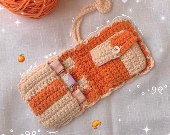 Puede incluir: Una bolsa de crochet a rayas naranja y crema con cierre de solapa. La bolsa está abierta y tiene varios billetes dentro.
