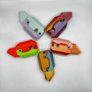Könnte beinhalten: Sechs bunte, vielseitige, geometrische Formen mit einem Sternburst-Design. Jede Form hat eine andere Farbe, darunter Lila, Orange, Grün, Blau, Rot und Hellblau.