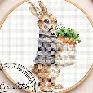 May include: Cross stitch pattern featuring a brown rabbit wearing a blue jacket, holding a bag of carrots. The design is set in a wooden embroidery hoop. The text "CG CrossStitch" and "Cross Stitch Patterns" is visible.