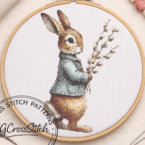 May include: A cross-stitch pattern of a brown rabbit wearing a blue-grey jacket, holding pussy willow branches. The design is set in a wooden embroidery hoop. The text "CROSS STITCH PATTERNS" and "CG CrossStitch" are visible.