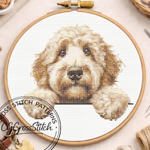 Puede incluir: Un patrón de punto de cruz de un perro golden doodle en un bastidor de madera. La cara y las patas del perro son visibles, con puntadas detalladas en tonos marrones y crema. El bastidor está sobre un fondo blanco, con suministros de artesanía en el fondo.