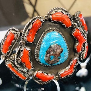 May include: A silver bracelet with a turquoise stone and coral accents.