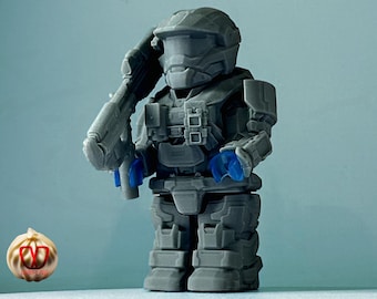 May include: A gray and blue plastic action figure of a soldier wearing a helmet and holding a gun. The figure is standing on a gray surface.