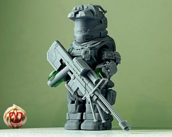 May include: A gray plastic action figure of a soldier wearing a helmet and holding a large gray rifle. The figure is standing on a white surface.