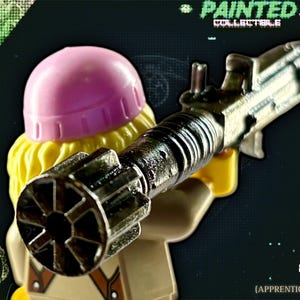 Peut inclure: Figurine de collection peinte tenant une arme métallique. La figurine a un casque rose, des cheveux jaunes et une tenue beige. L'image comprend le texte "PAINTED COLLECTIBLE" et "Star Seller (Apprentice Grade)".