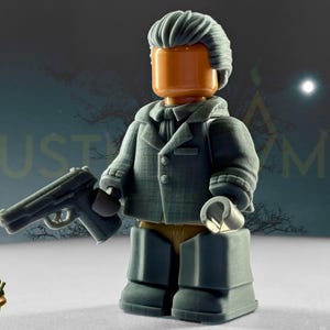 May include: A gray toy figure of a man in a coat holding a gun and a metal object. The figure has a gray wig and an orange head. The background is a dark, snowy scene with the text "JUST A GAME".