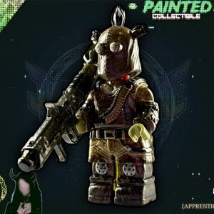 Op de afbeelding: Een bruin en goud geschilderd verzamelobject van een personage met een helm, een bril en een groot geweer. De figuur draagt een riem en heeft een bandolier. De achtergrond is donkergroen met de tekst "PAINTED COLLECTIBLES" en "JUSTMYGVMIE".