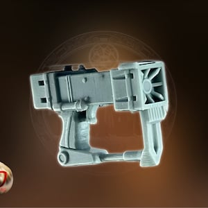 May include: A gray plastic sci-fi weapon with a detailed design. The weapon has a barrel with a fan-like structure and a handle with a trigger.