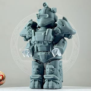 May include: A gray 3D printed figurine of a robot wearing a helmet and armor. The robot has a detailed design with visible gears and joints.