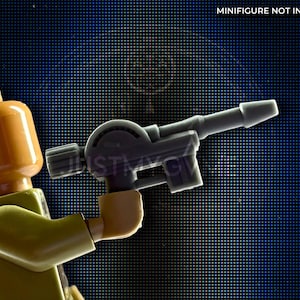 Puede incluir: Una minifigura de Lego de color beige y verde oliva sosteniendo una pistola bláster gris. La minifigura tiene una cabeza beige y un torso y brazos verdes. La pistola bláster es gris y tiene un cañón largo. El fondo es azul oscuro con un patrón de cuadrícula. El texto en la esquina superior derecha dice "MINIFIGURE NOT INCLUDED."